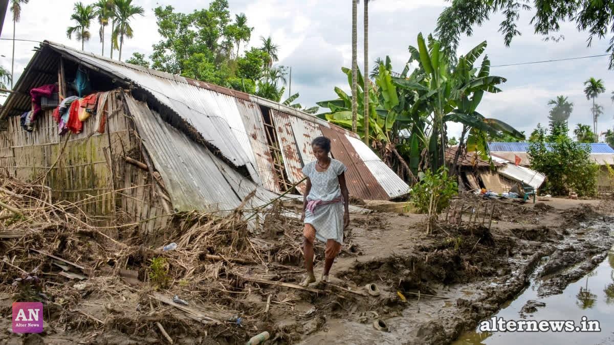 A woman walks past a damaged house amid mud and debris, in Sivasagar district of Assam. (PTI)